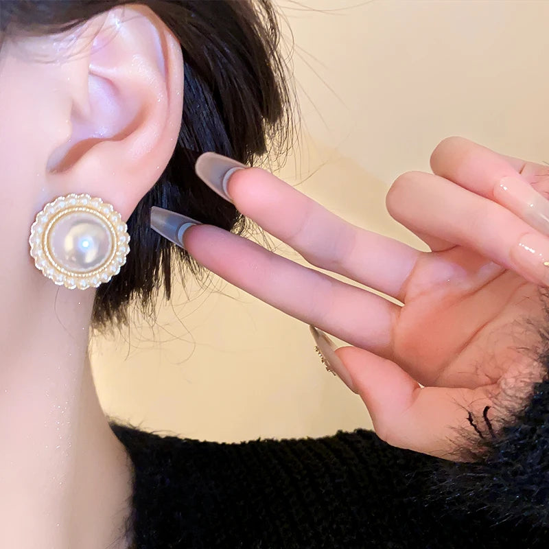 Boucles d’oreilles Euphémia en acier inoxydable doré, ornées d’une grosse perle entourée de perles délicates, portées avec élégance.
