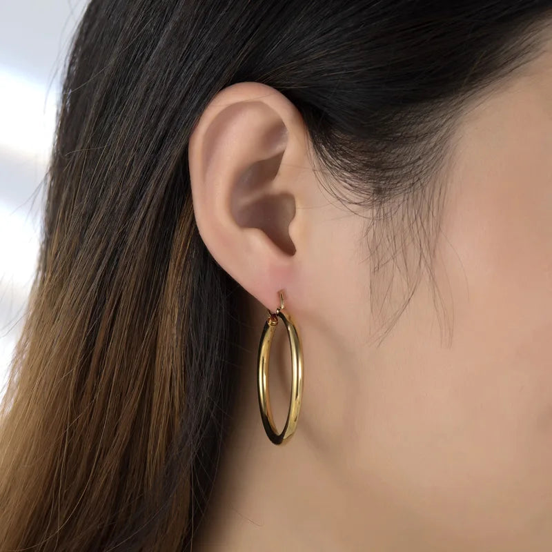 Boucles d’oreilles créoles épaisses dorées en acier inoxydable portées par une femme – style audacieux et moderne.