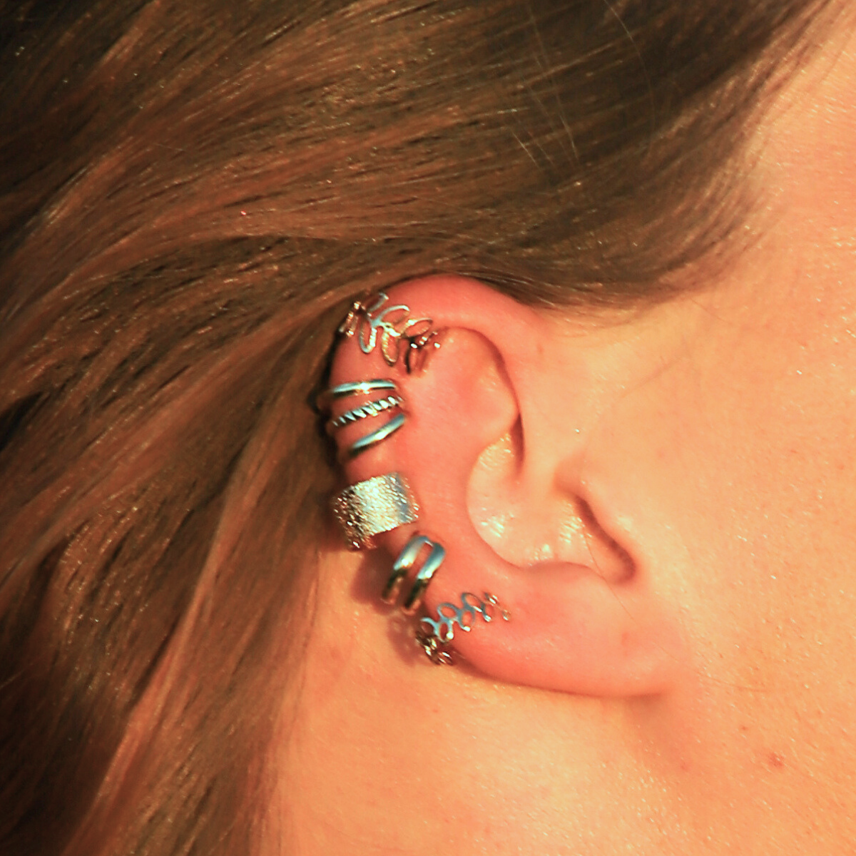 Gros plan sur une oreille avec 5 earcuffs dorés portés, sans perçage, en acier inoxydable