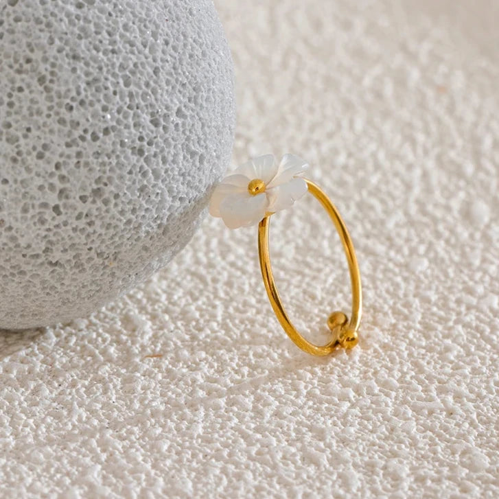 Zoom sur la bague Eurynome en acier inoxydable doré, mettant en valeur sa fleur blanche lumineuse et son design fin et élégant.