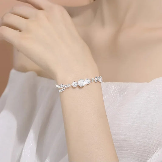 Bracelet Élixir Divin argenté en acier inoxydable, composé de trois joncs entrelacés avec perles ciselées, porté pour un look raffiné.