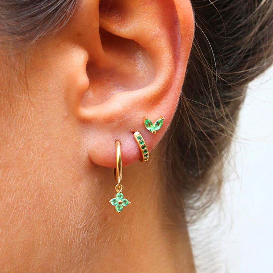 Boucles d’oreilles Cléophée dorées, ornées de strass verts scintillants, portées avec raffinement.
